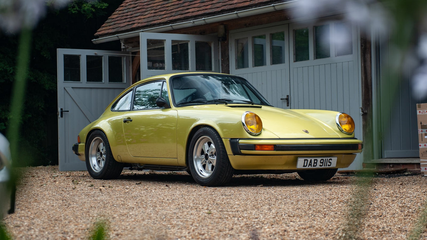 Our Porsche 911 SC in Delphi Green with silver Fuchs alloy wheels parked in front of a workshop 