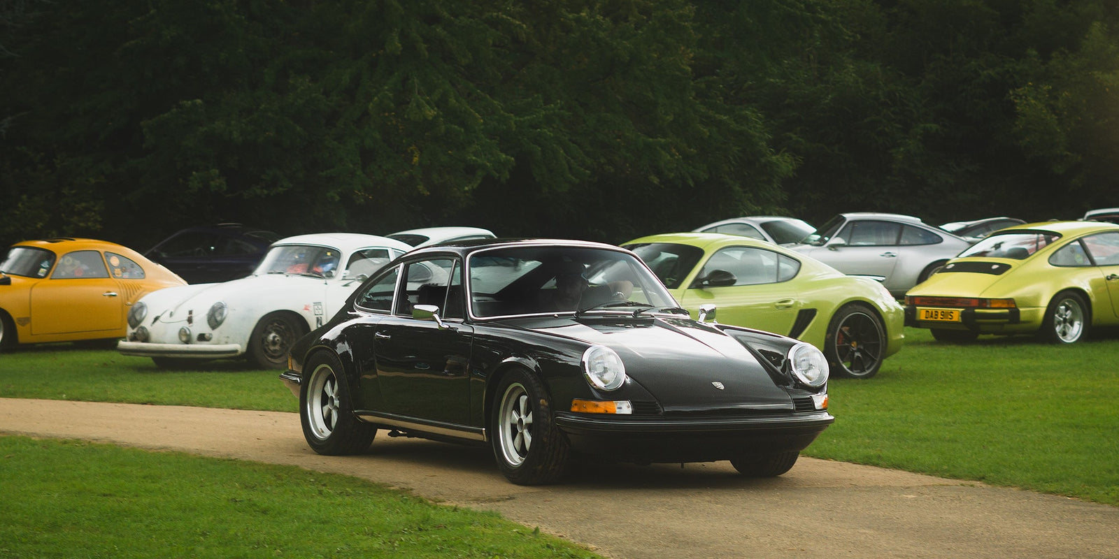 A black classic Porsche 911 surrounded by a variety of different 911's in a field at a Porsche classic car show